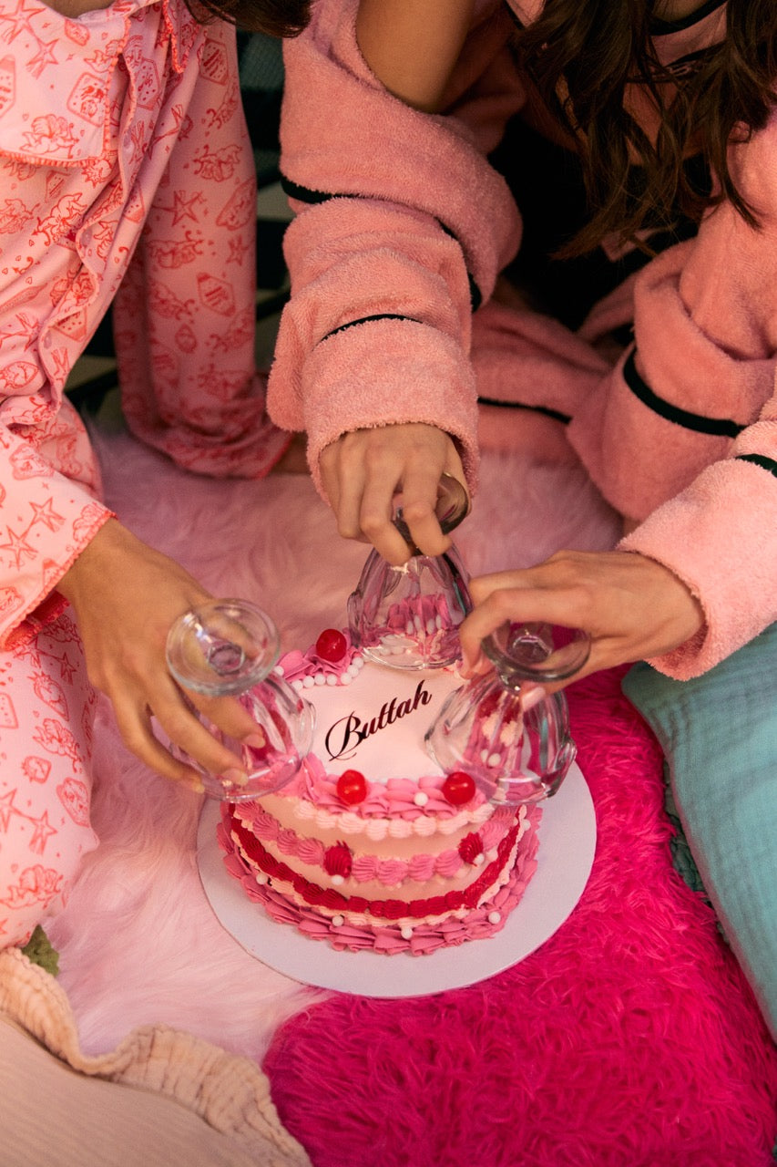 Three people in pink pajamas sitting on a pink rug with a cake in front of them.
