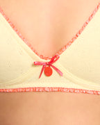 Close-up of a yellow Everyday Bra by Buttah with pink trim and a red bowtag on a beige background