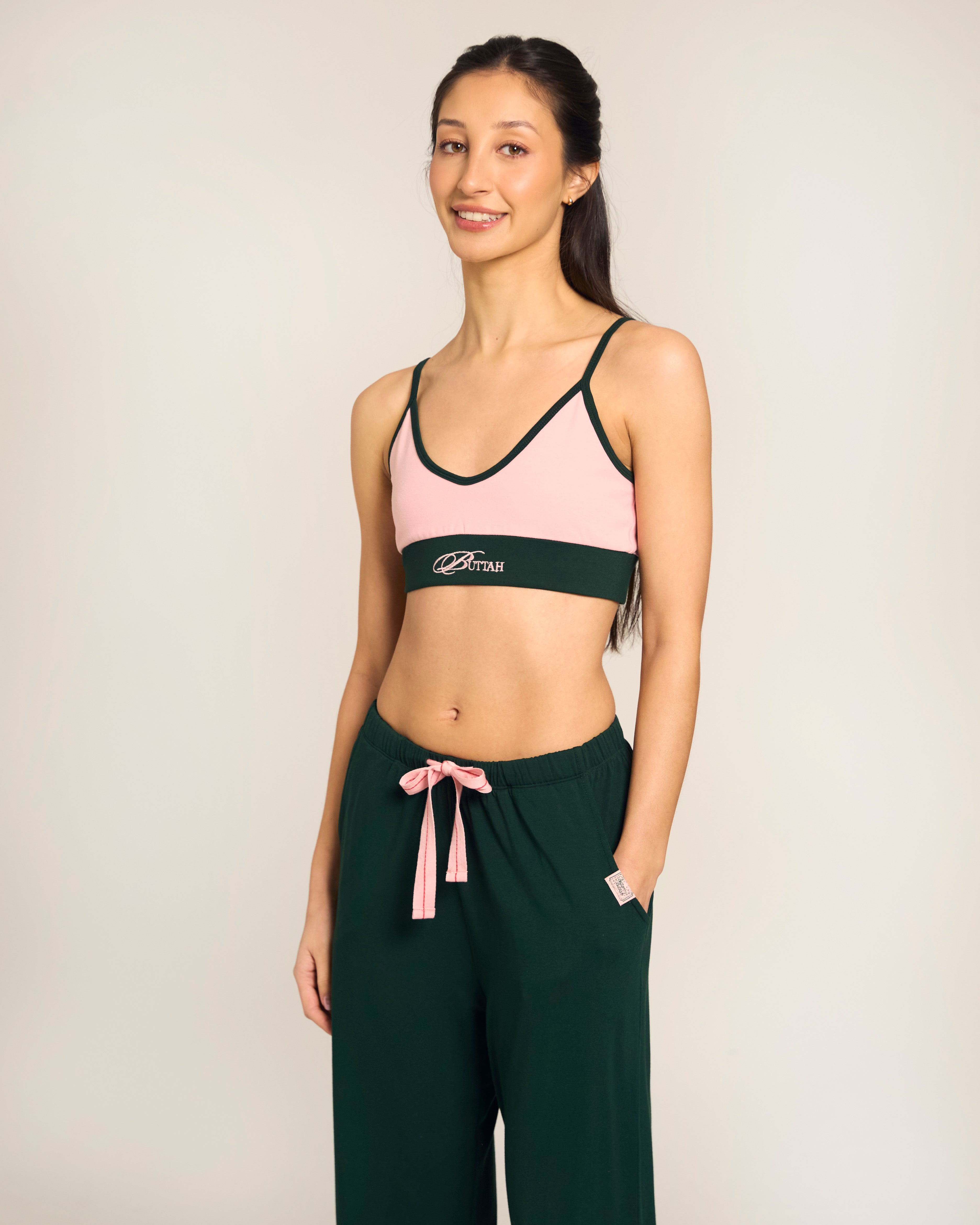Woman wearing a pink sports bra and green pants with a visible Buttah logo on a plain background