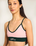 Woman wearing a pink sports bra by Buttah with green straps on a plain background