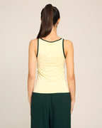 Woman wearing a Yellow Heartbreaker Tank by Buttah and dark green pants on a beige background - back view