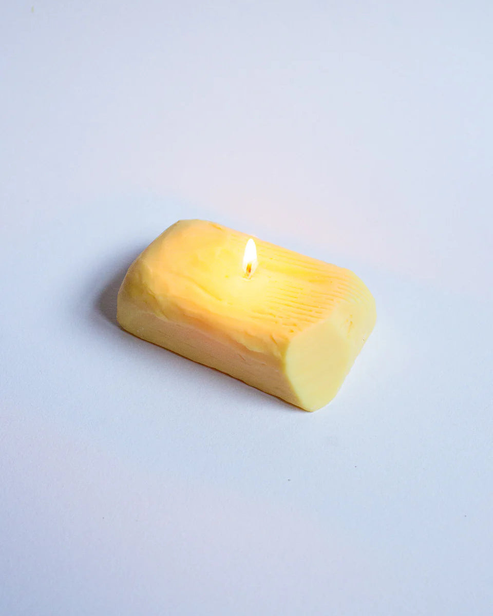 Butter candle with a lit wick on a light gray background